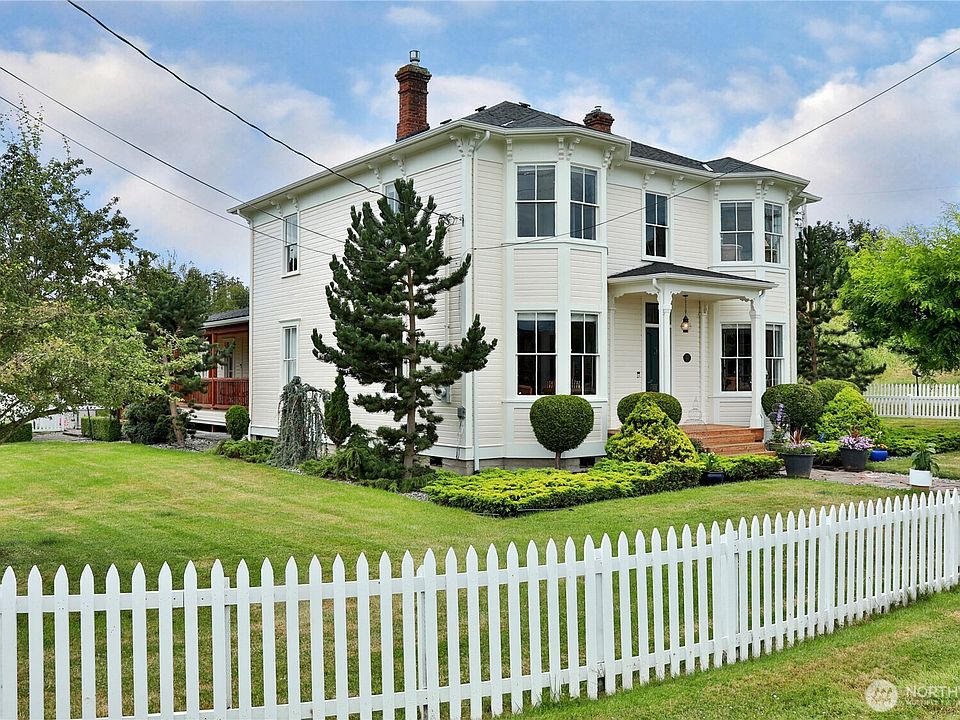 Side angle of the Italianate Victorian with the original Monterey pine and white picket fence under blue sky